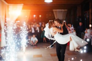 Groom carrying the bride as they kiss on the dance floor with fireworks behind them