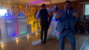 Wedding host inviting guests onto the dance floor with the bride and groom behind him