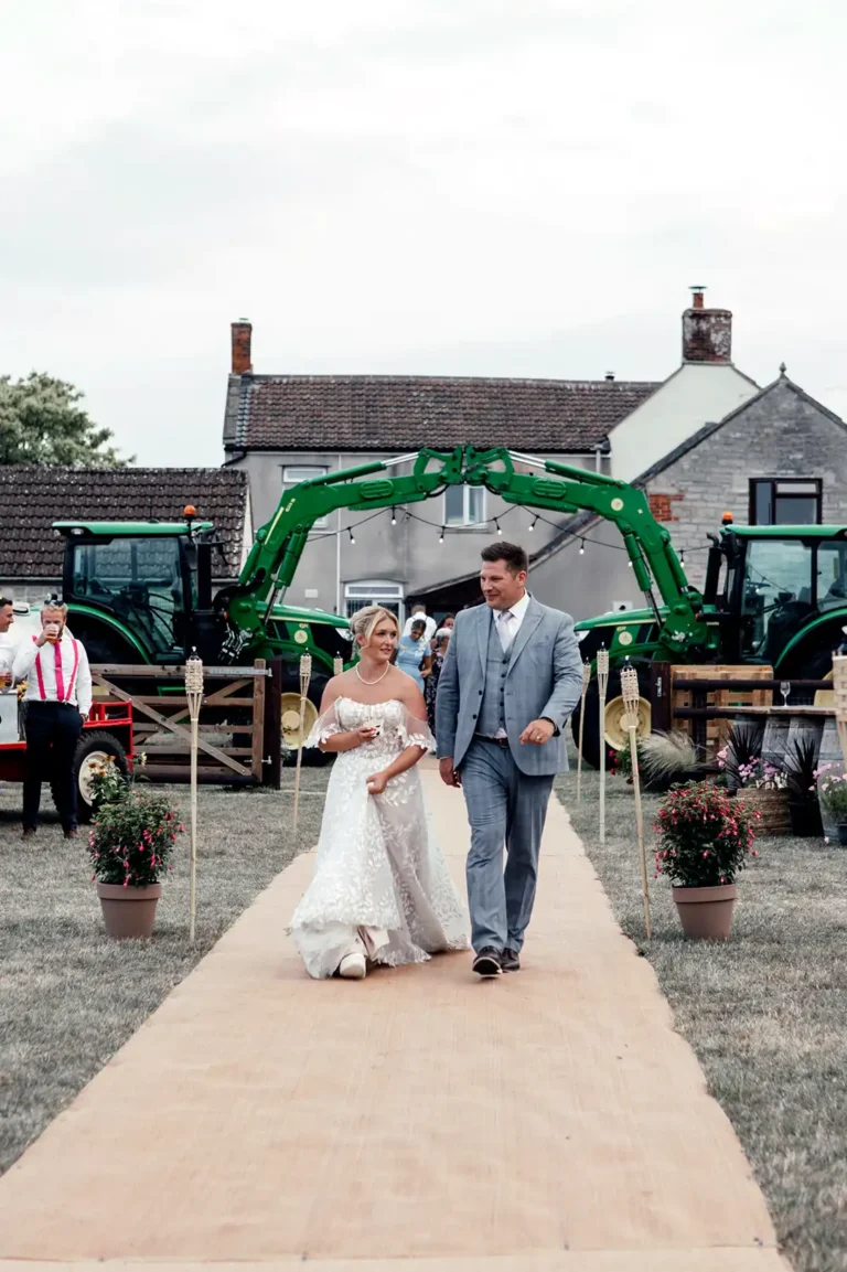 Wedding host walking with the bride along an outdoor aisle at a farm wedding.
